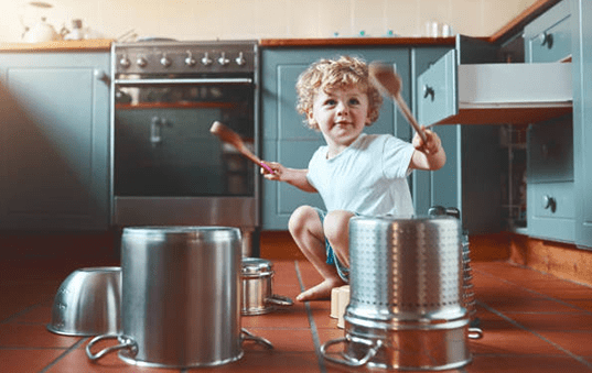 Young boy using wooden spoons as drumsticks while hitting pots on the kitchen floor of his home
