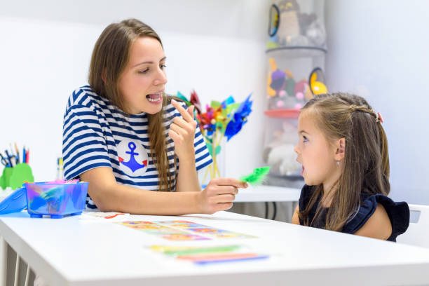 Speech Pathologist points to her mouth while working 1 on 1 with young girl during a therapy session