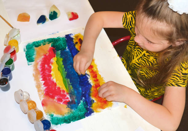 Little girl uses her creativity to paint a picture using several different colors and foam sponge
