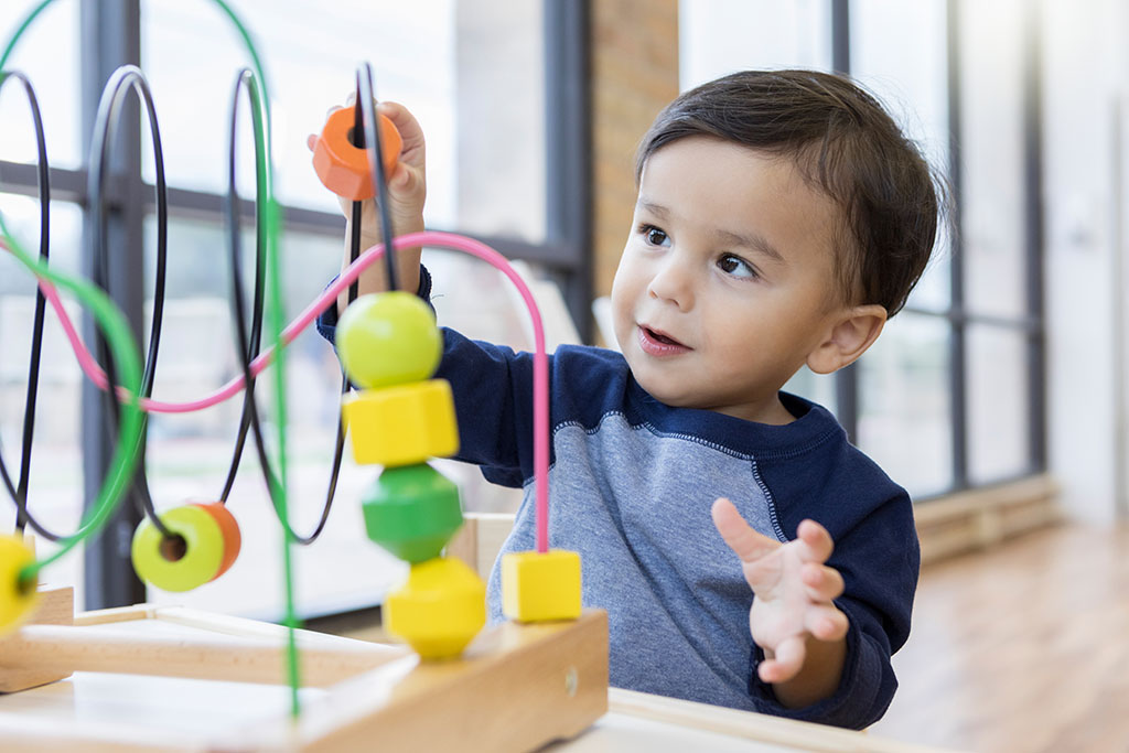 Adorable toddler boy plays with a bead roller coaster in the waiting room of a doctor's office.