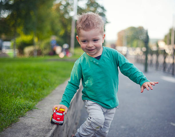 Boy wearing green shirt smiles while playing with his toy truck outside at the park