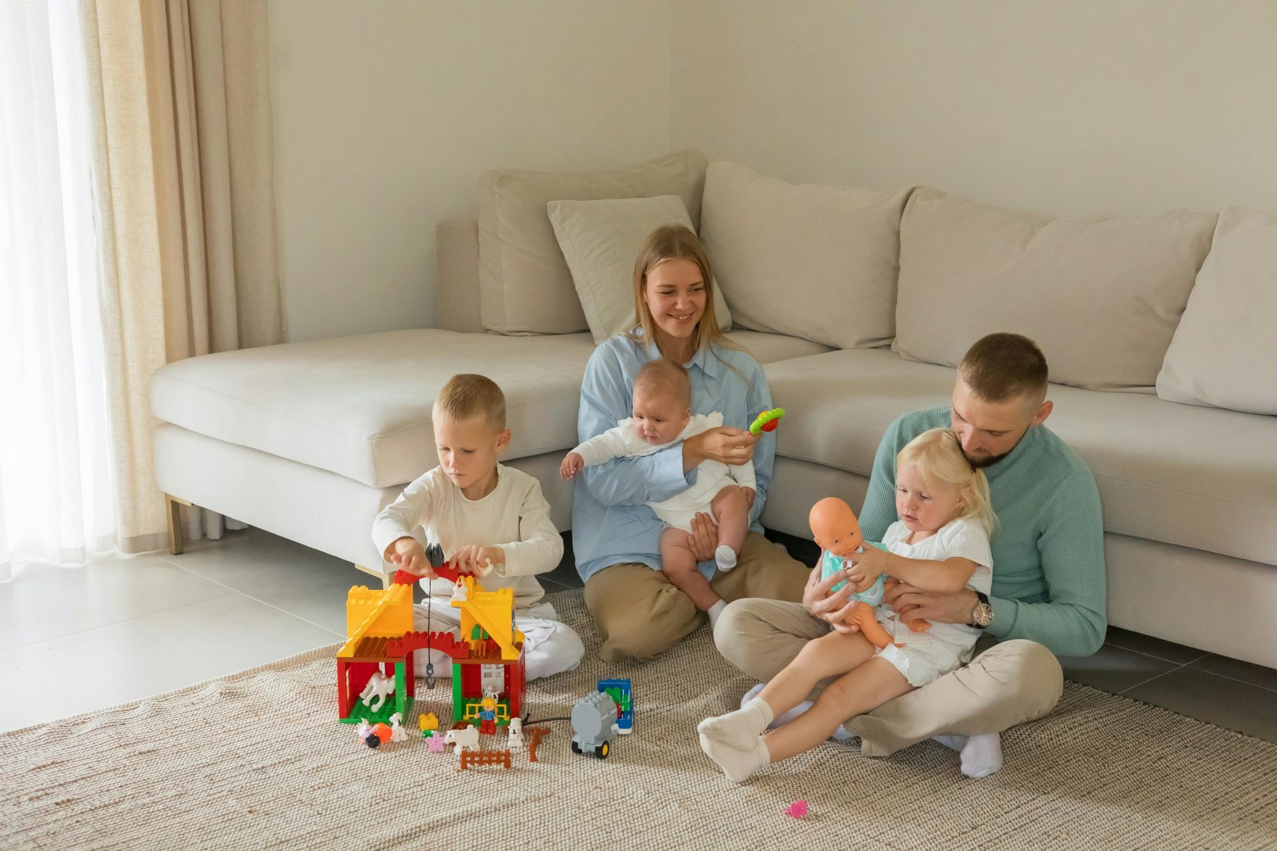 Parents sit on the floor with their children playing with building blocks. Parent involvement in ABA therapy.